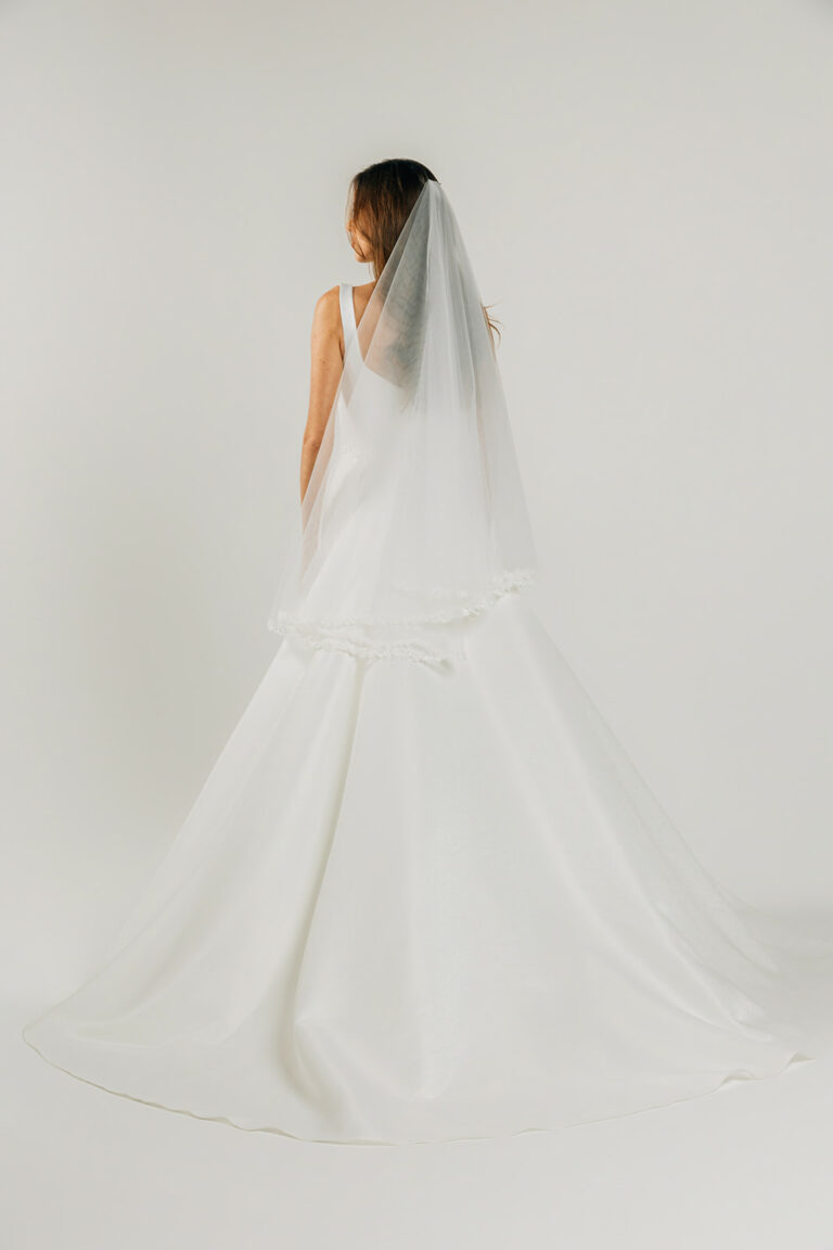 femme dans une robe de mariée A-line épurée avec un sac en perle et un voile